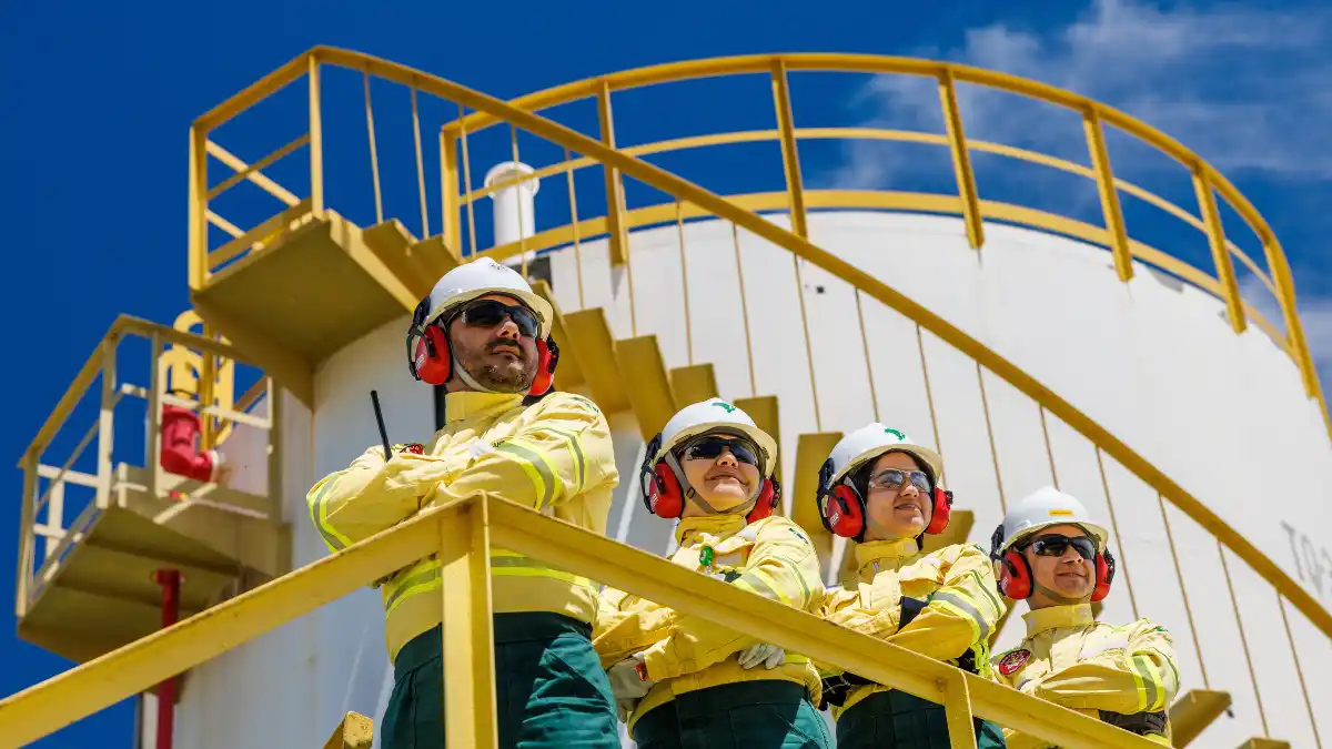 Quatro profissionais em uniformes de segurança amarelos e capacetes em uma plataforma industrial, simbolizando a operação da PetroRecôncavo.