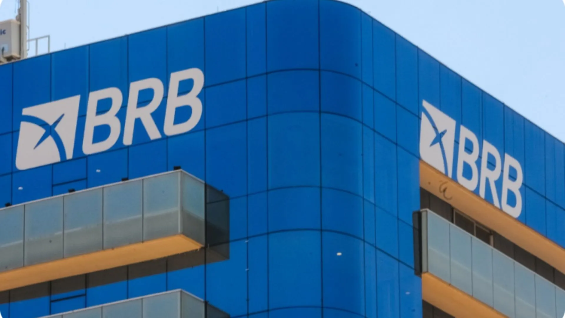 Fachada do edifício do BRB (Banco de Brasília), com logotipo em destaque sobre painéis de vidro azul, representando a sede moderna da instituição financeira.