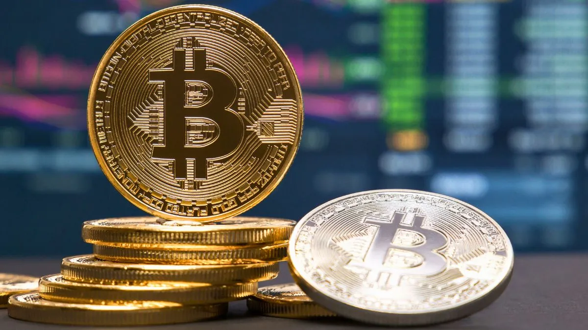 Moedas de Bitcoin com gráfico financeiro ao fundo, representando a alta do Bitcoin