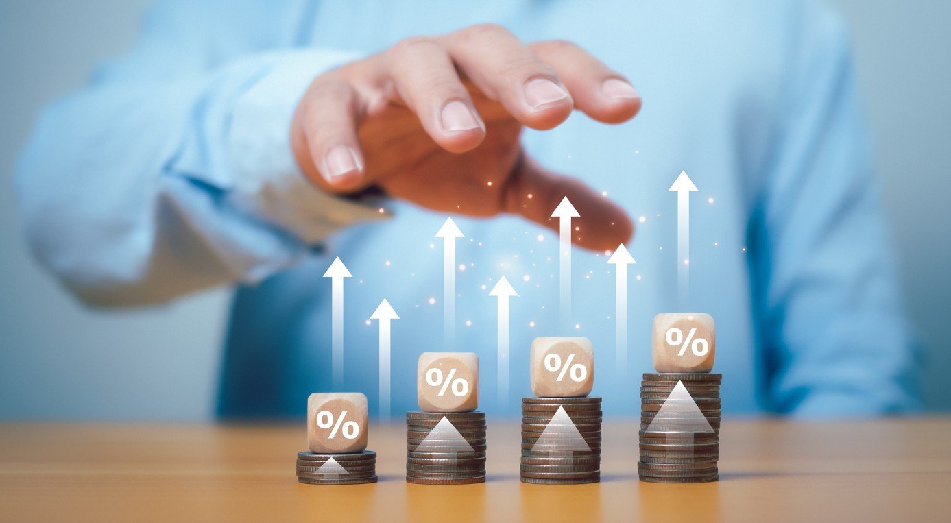 dividendos maiores que a Selic: imagem de mão de homem analisando setas para cima sobre pilhas de moedas