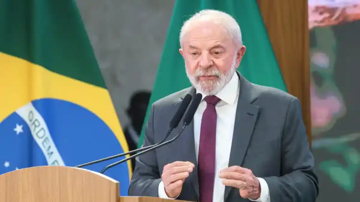 Presidente Lula discursando em um pódio, com as bandeiras do Brasil e de uma organização internacional ao fundo.