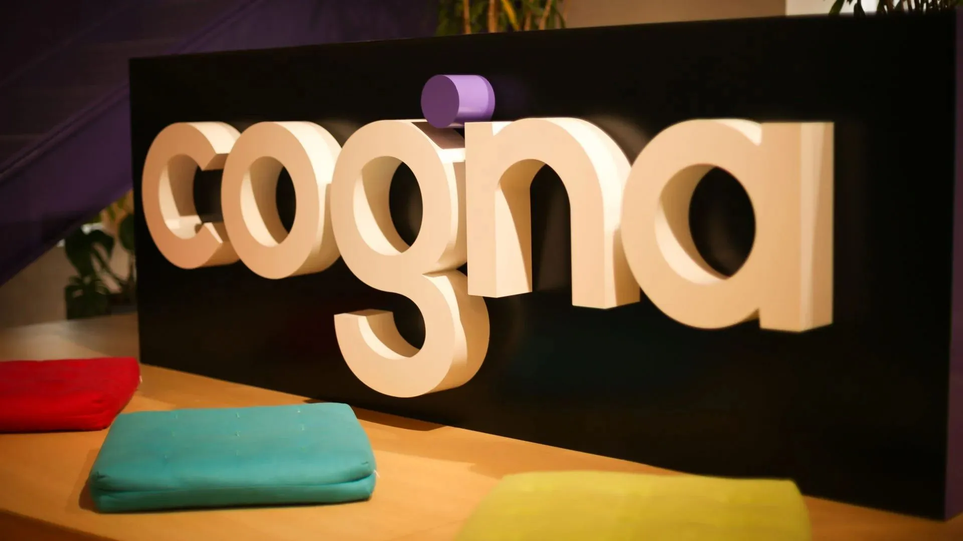 Logo da Cogna em ambiente institucional com fundo colorido, usada em divulgação de resultados financeiros