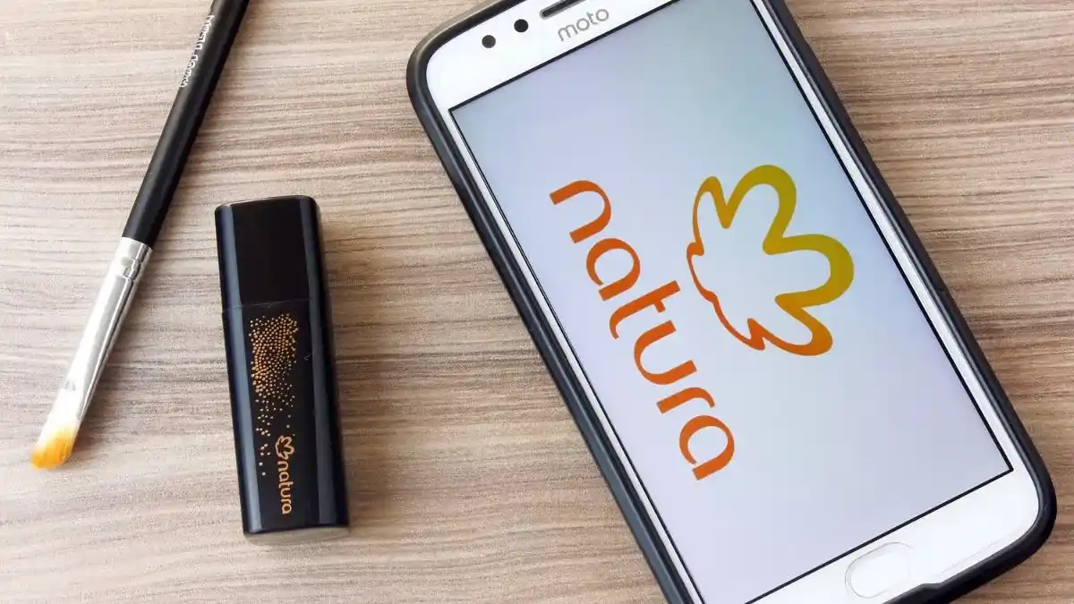 Celular com o logotipo da Natura e produtos de maquiagem, simbolizando a incorporação.