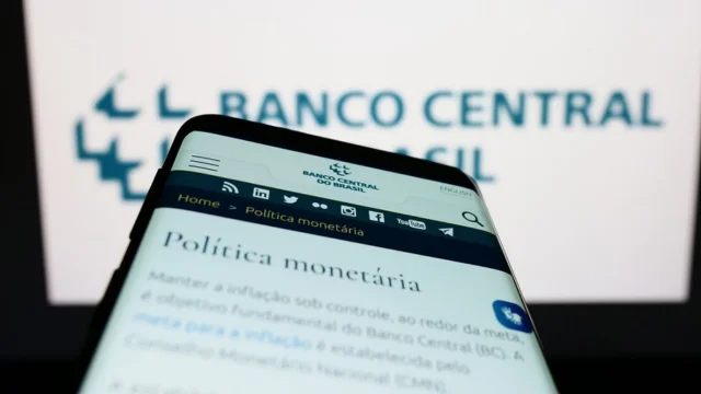 Tela de celular exibindo a página do Banco Central e o texto "Política Monetária", simbolizando a Selic mantida em 15% e as oportunidades de investimento com juros parados.