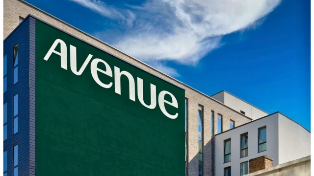 Logotipo da Avenue em destaque em uma grande parede verde de um edifício corporativo moderno sob um céu azul, representando a presença da Avenue Institucional.