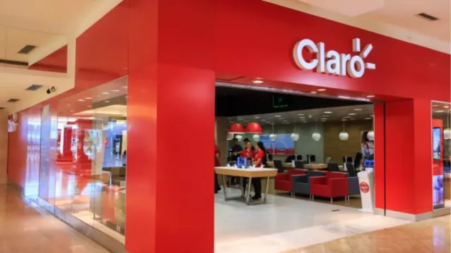 Fachada de vidro de um edifício corporativo com o logotipo circular vermelho e branco da Claro em destaque, representando a empresa na aquisição da Desktop Claro.