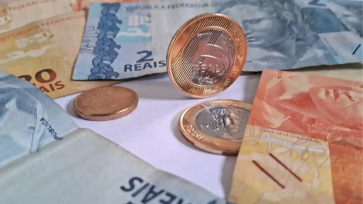 Moedas e notas de Real (R$ 2, R$ 10, R$ 1,00) espalhadas em uma mesa, representando as contas públicas e o déficit primário do setor público.