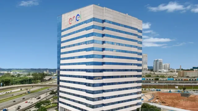 Vista externa de um moderno edifício corporativo envidraçado com o logotipo da Enel em destaque no topo, representando a infraestrutura da Enel São Paulo.